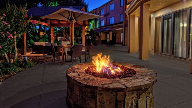 An outdoor patio area with a stone fire pit, outdoor seating, and a building in the background. - Courtyard by Marriott Abilene Southwest/Abilene Mall South (Abilene)