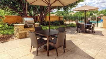 An outdoor patio with a grill, dining table, chairs, and umbrellas.