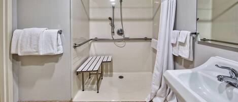 Un baño con ducha a nivel, un banco, un lavabo y un espejo.