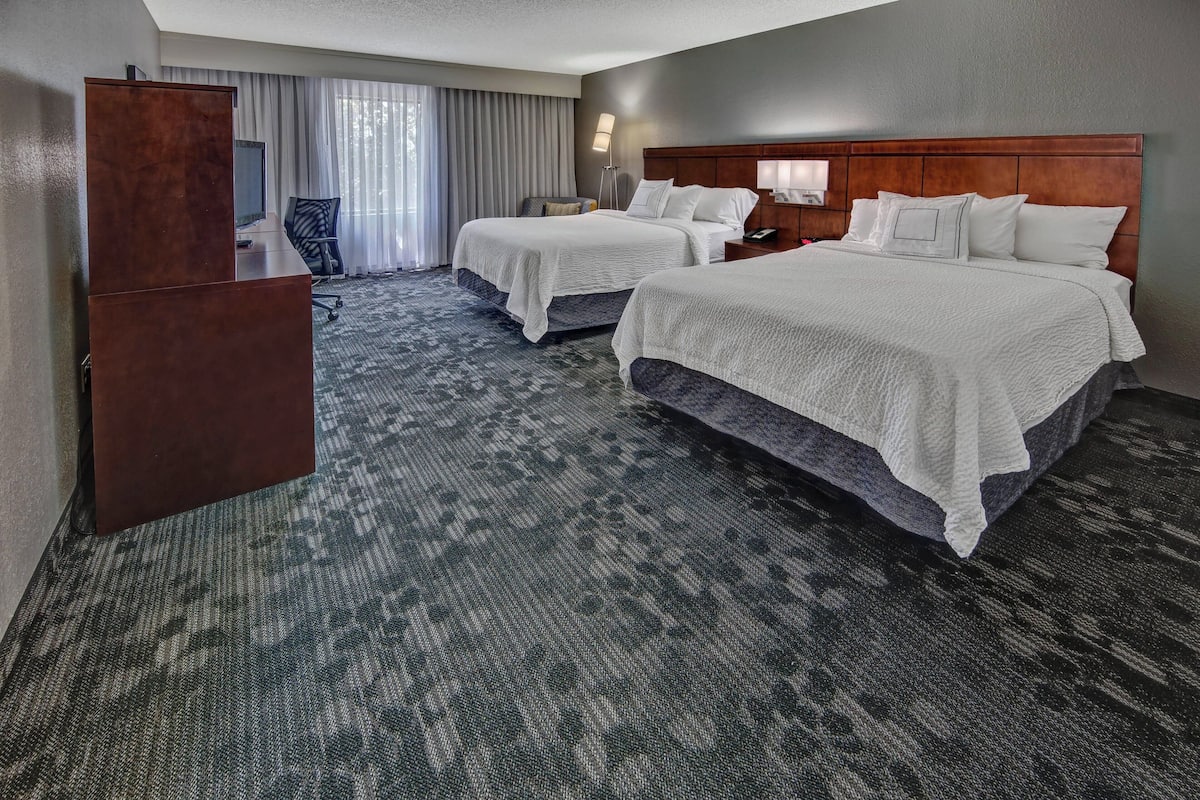 A hotel room with two beds, a desk, a chair, and a large window with curtains.