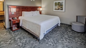 Habitación de hotel con una cama grande, una mesita de noche con un teléfono, una silla y un cuadro en la pared.