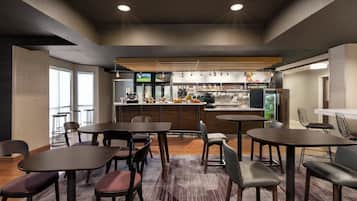 Un moderno vestíbulo de hotel con varias zonas de estar, un bar y una cocina a la vista.