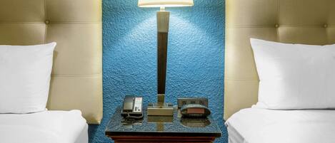 A hotel room with a bed, a nightstand with a lamp, a telephone, and a power outlet.