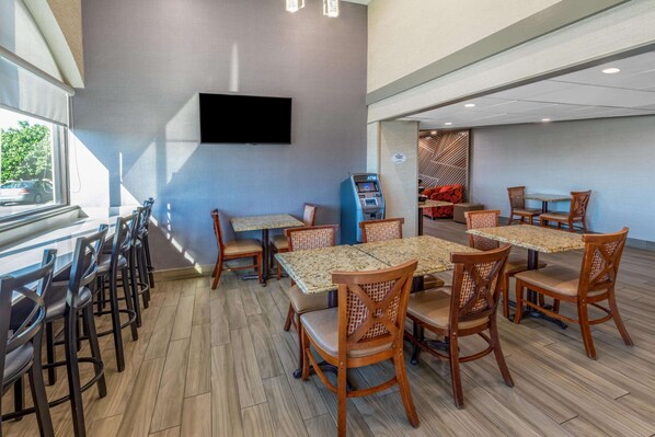 A modern dining area with multiple tables and chairs, a flat-screen TV mounted on the wall, and an ATM machine. - Baymont by Wyndham McAllen/Pharr (McAllen)
