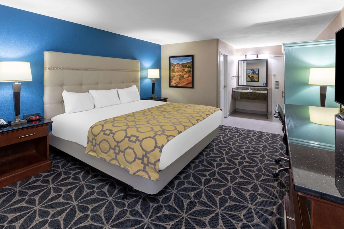 Habitación de hotel con una cama grande, una mesita de noche, un escritorio, un espejo y un baño con lavamanos y espejo.