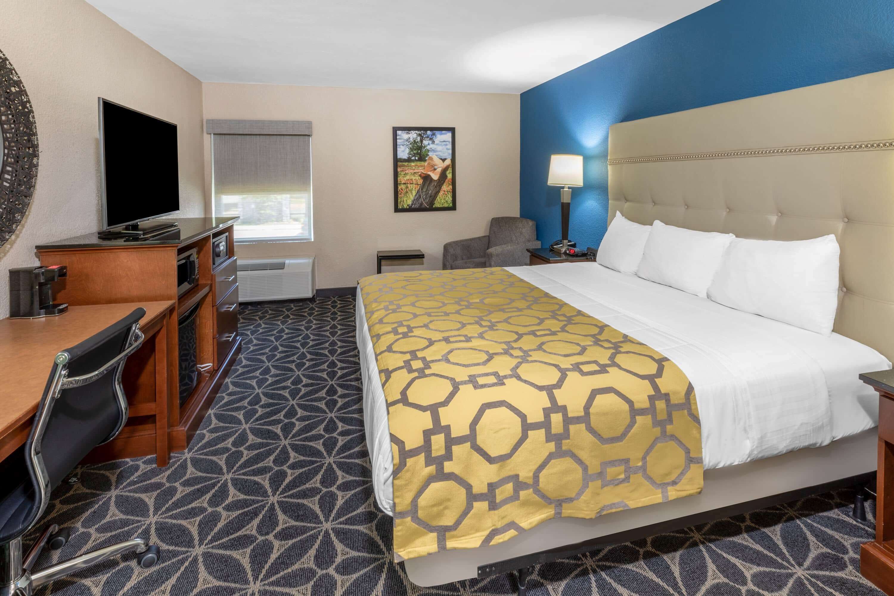 A hotel room with a bed, a desk with a chair, a TV, and a window with blinds.