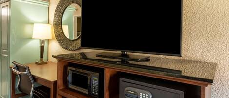 A hotel room with a flat-screen TV, a microwave, a safe, and a desk with a chair.