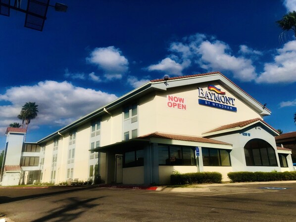Un hotel con un letrero que dice 'ABIERTO' y un letrero de 'Baymont by Wyndham', además de un estacionamiento.