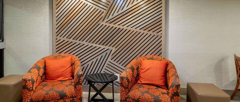 Una habitación con dos sillones, una mesita y un panel decorativo en la pared.