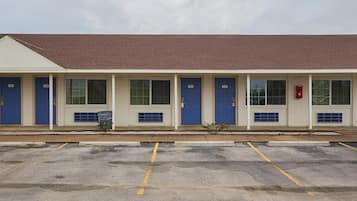 Un motel con seis puertas azules numeradas del 104 al 110, un buzón rojo y un estacionamiento con líneas amarillas.
