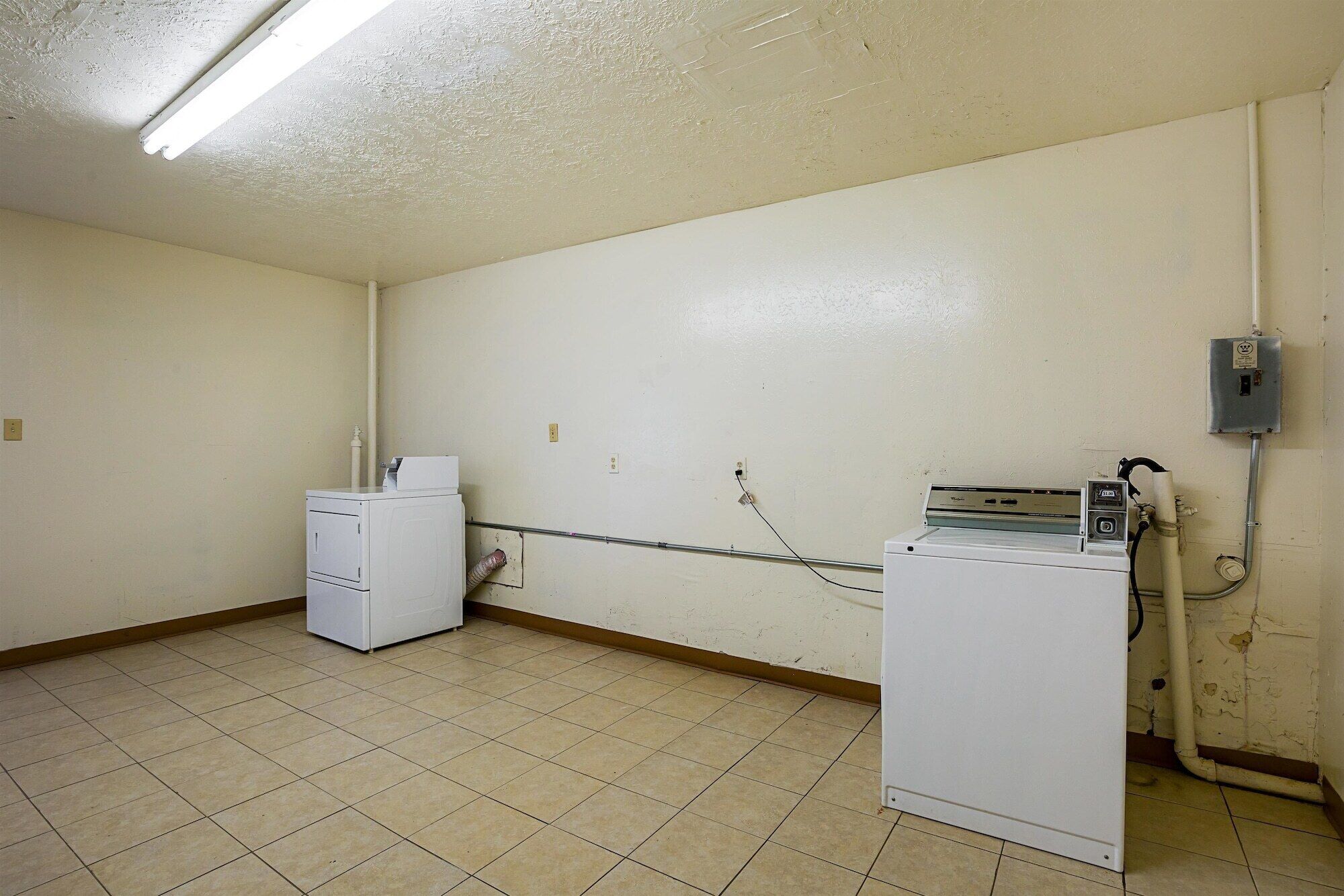 A laundry room with two washing machines, a dryer, and a utility meter on the wall.