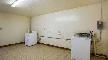 A laundry room with two washing machines, a dryer, and a utility meter on the wall.