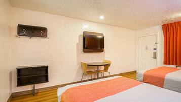 A hotel room with two beds, a TV mounted on the wall, a small table with chairs, and a coat rack.