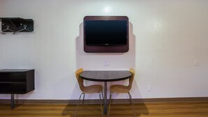 Una habitación pequeña con una mesa redonda, dos sillas, un televisor montado y un perchero.