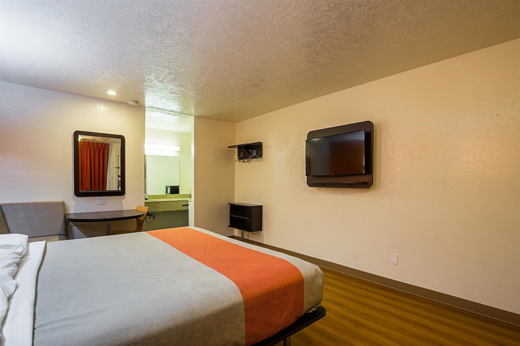 A hotel room with a bed, a chair, a desk, a television, and a mirror.