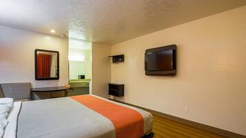 A hotel room with a bed, a chair, a desk, a television, and a mirror.