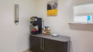 Una cafetera, una cesta con utensilios y un cuadro en una encimera.