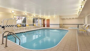 An indoor swimming pool with tiled flooring, yellow lounge chairs, and a ceiling with recessed lighting.