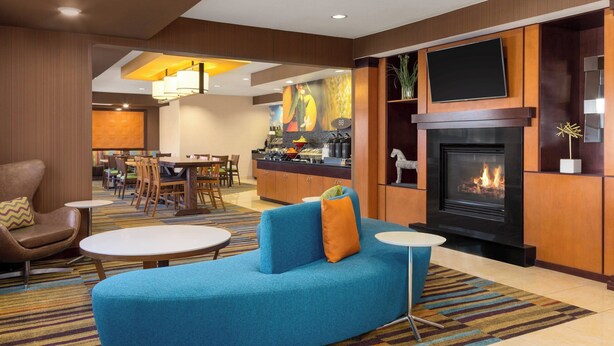 A hotel lobby with a blue sofa, a fireplace, a dining area, and a TV mounted on the wall.