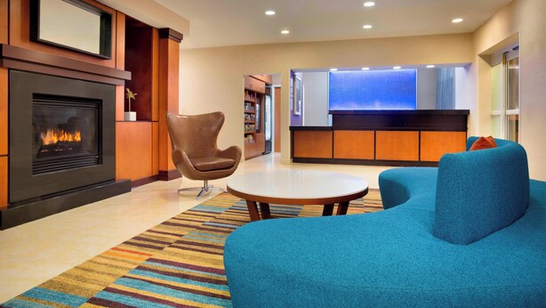 A modern lobby with a fireplace, seating area, and a kitchen in the background. - Fairfield Inn & Suites by Marriott® Dallas Plano West (Plano)