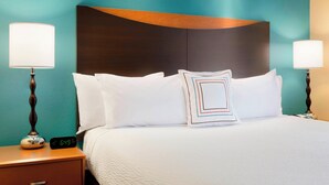 A hotel room with a bed, two bedside lamps, a digital clock, and teal walls. - Fairfield Inn & Suites by Marriott® Dallas Plano West (Plano)