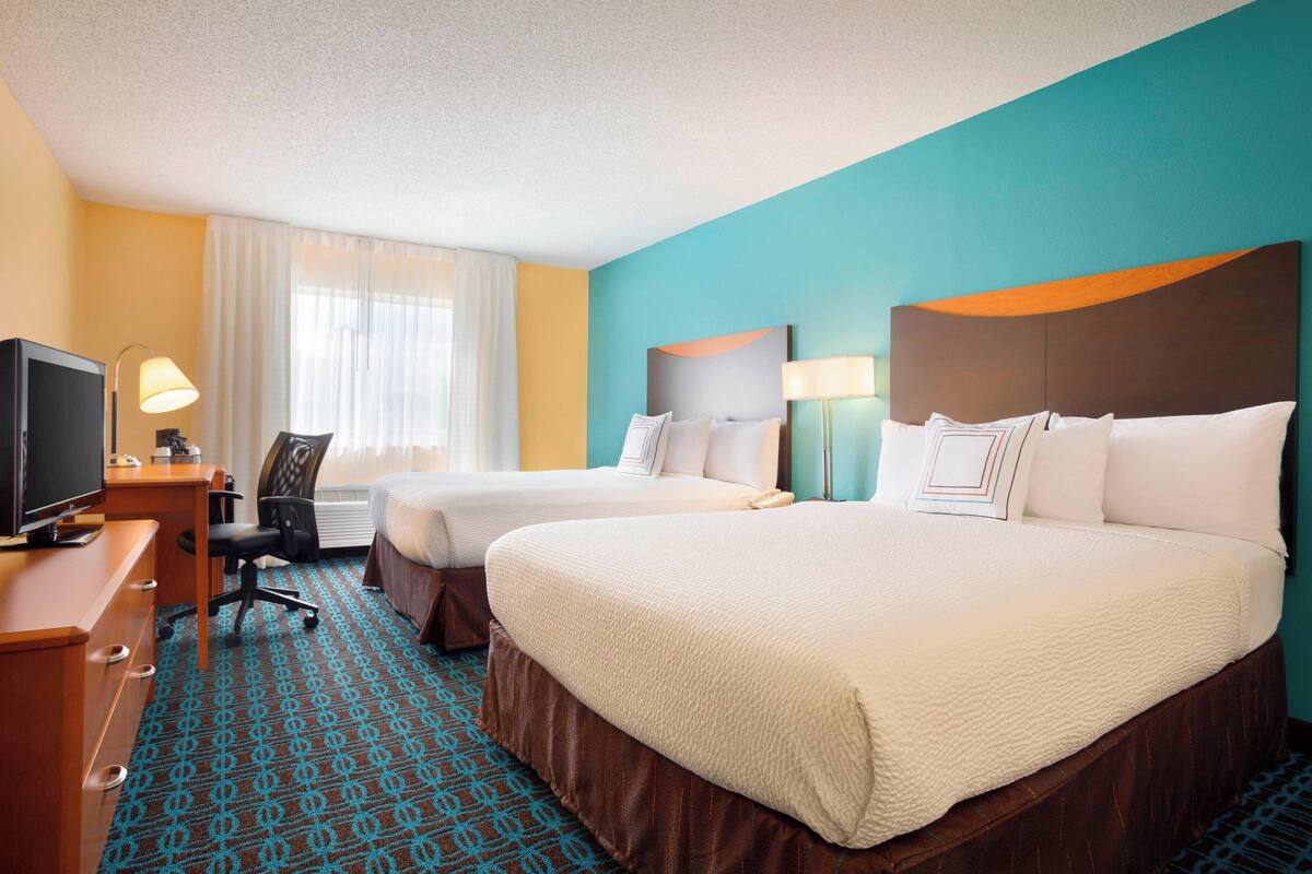 A hotel room with two beds, a desk with a TV, and a chair.