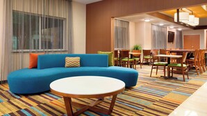 A modern hotel room with a blue sofa, a round table, and a dining area with wooden chairs and a small table. - Fairfield Inn & Suites by Marriott® Dallas Plano West (Plano)