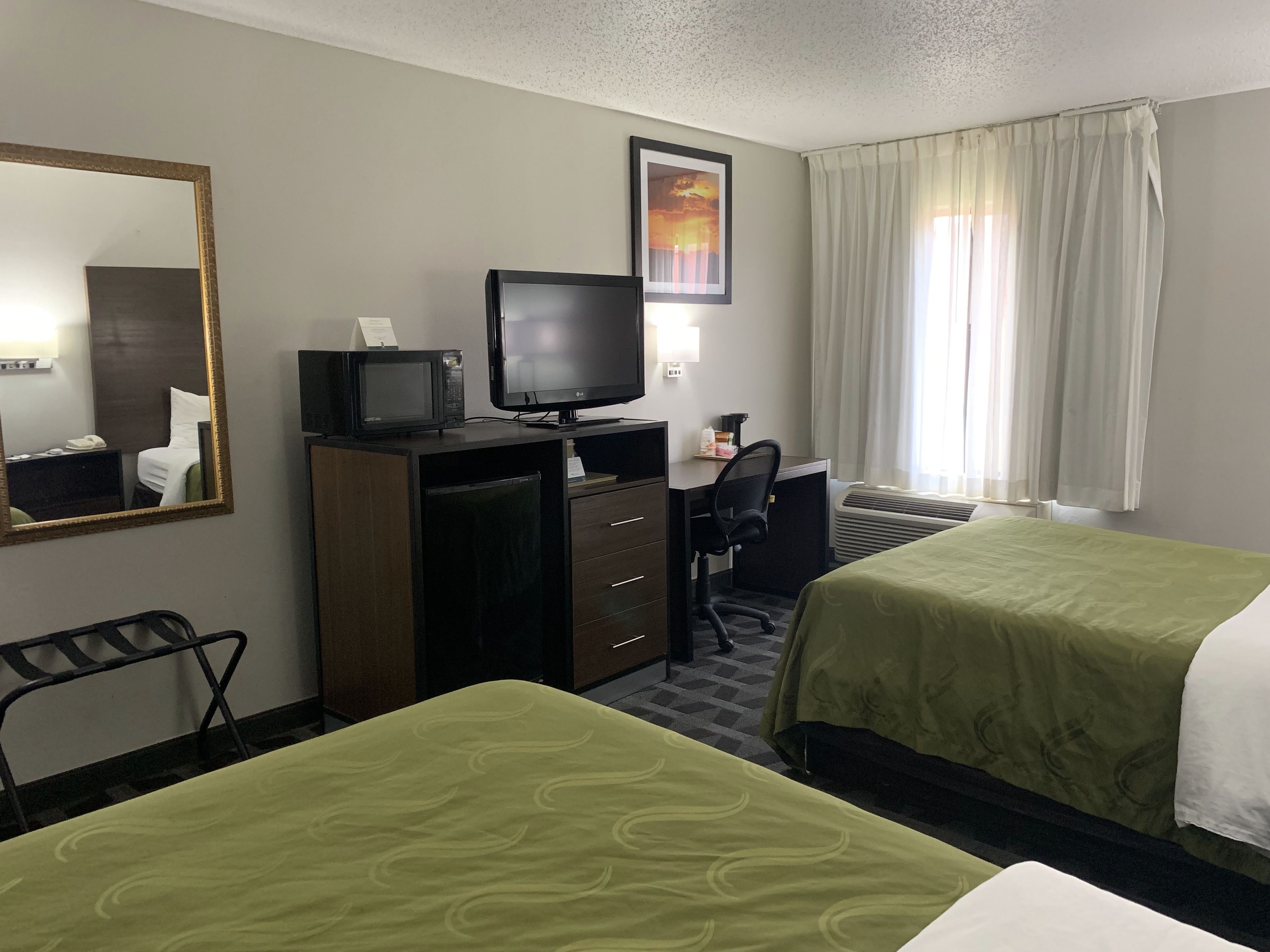Quarto de hotel com duas camas, uma mesa de escritório com computador, televisão, micro-ondas e um espelho grande.