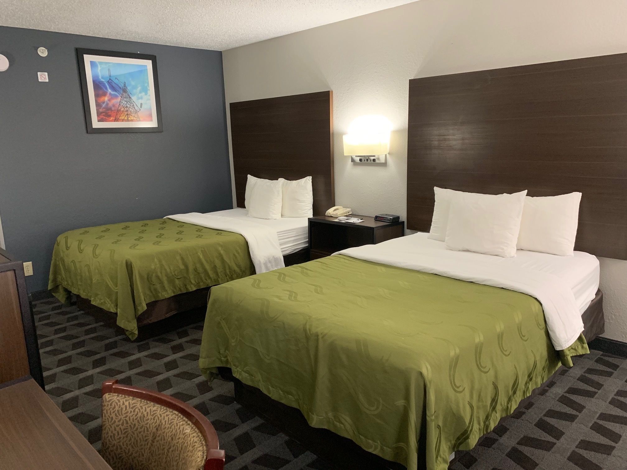 Una habitación de hotel con dos camas, una mesita de noche, una lámpara y un cuadro en la pared.