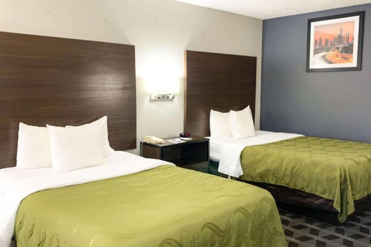 A hotel room with two beds, a nightstand with a phone, and a cityscape picture on the wall.