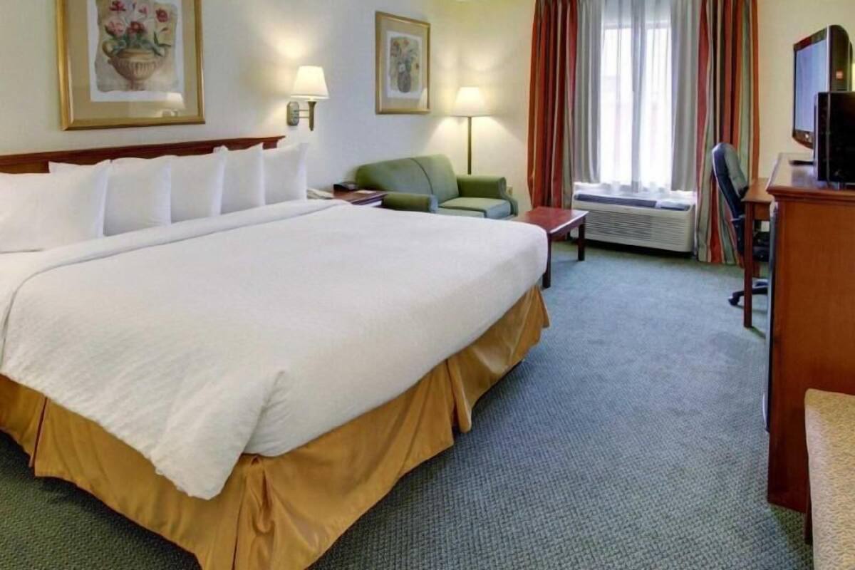 A hotel room with a large bed, a desk, a chair, a television, and two lamps.