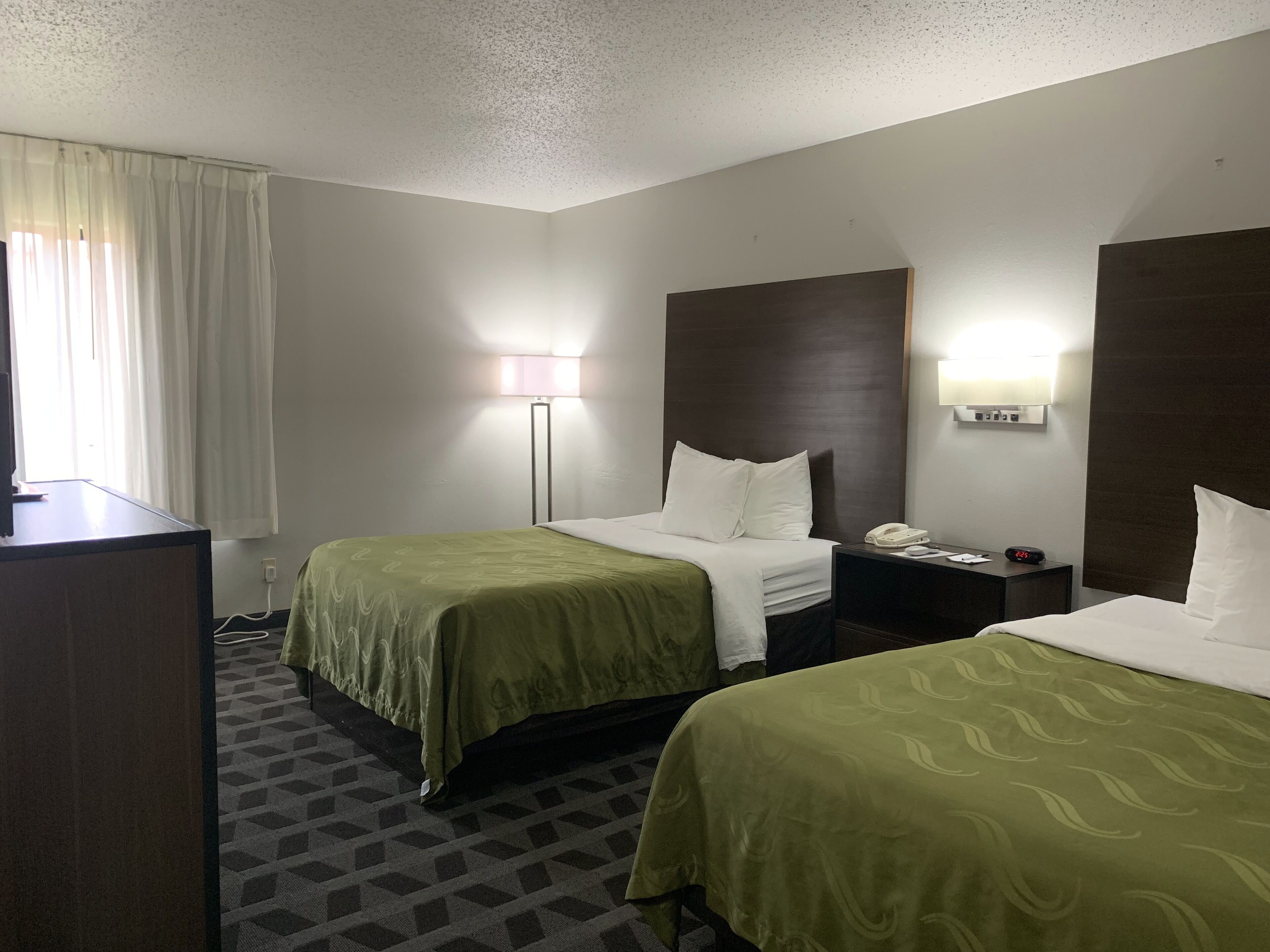 A hotel room with two beds, a desk, a lamp, a nightstand, and a telephone.