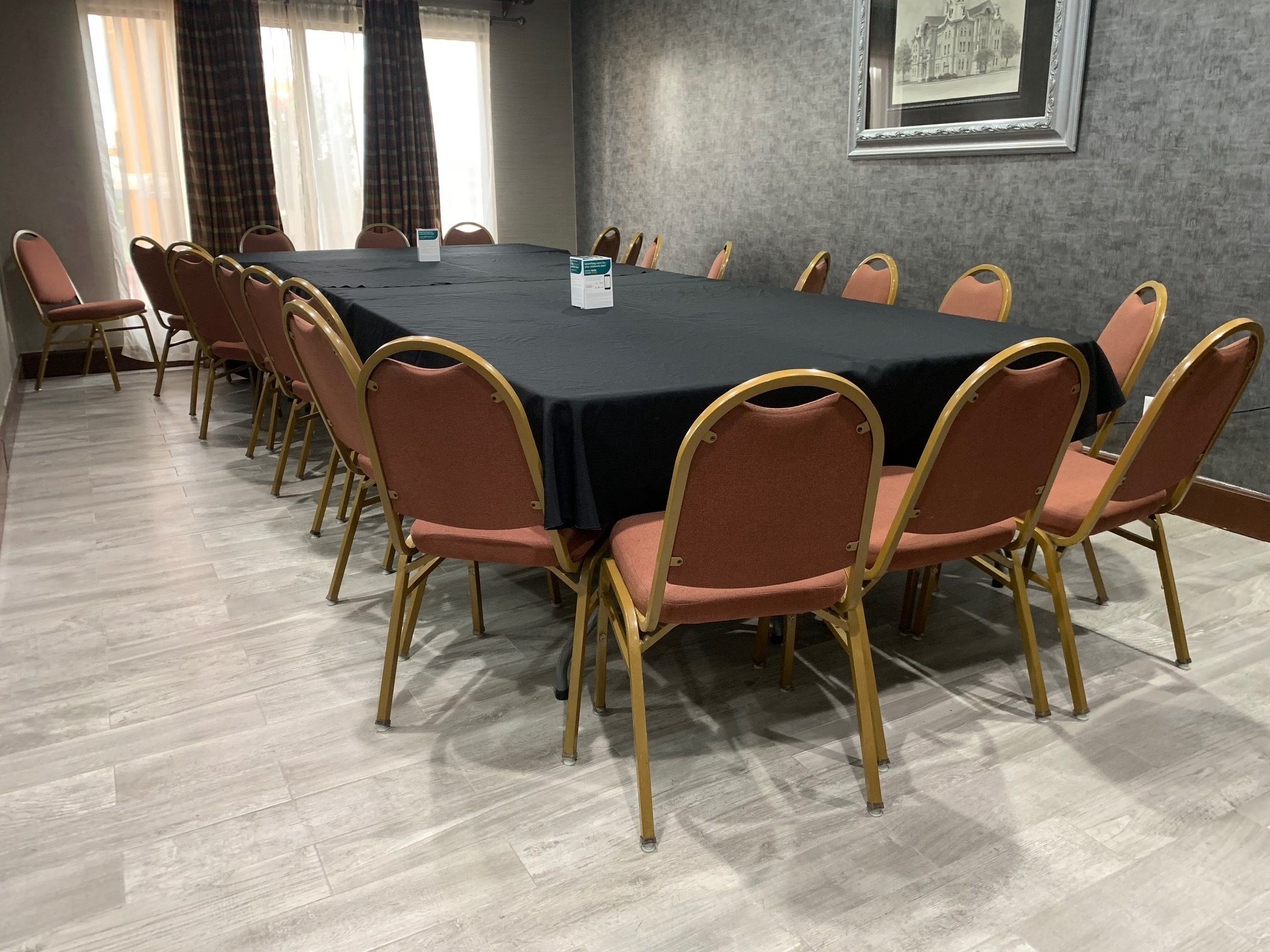 A conference room with a long table and chairs, a framed picture on the wall, and a window with curtains.