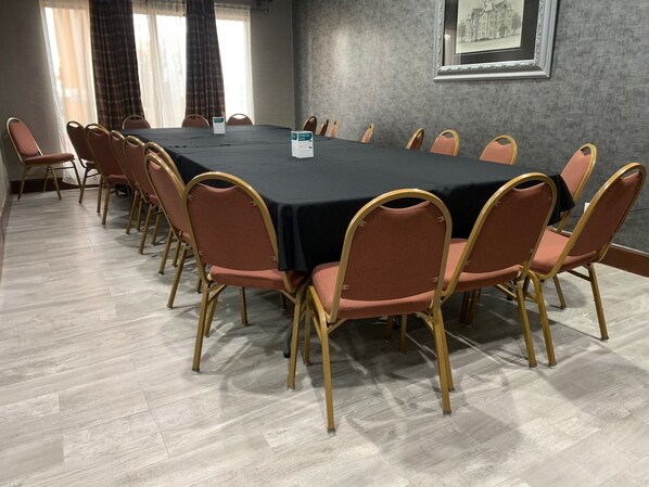 A conference room with a long table and chairs, a framed picture on the wall, and a window with curtains.