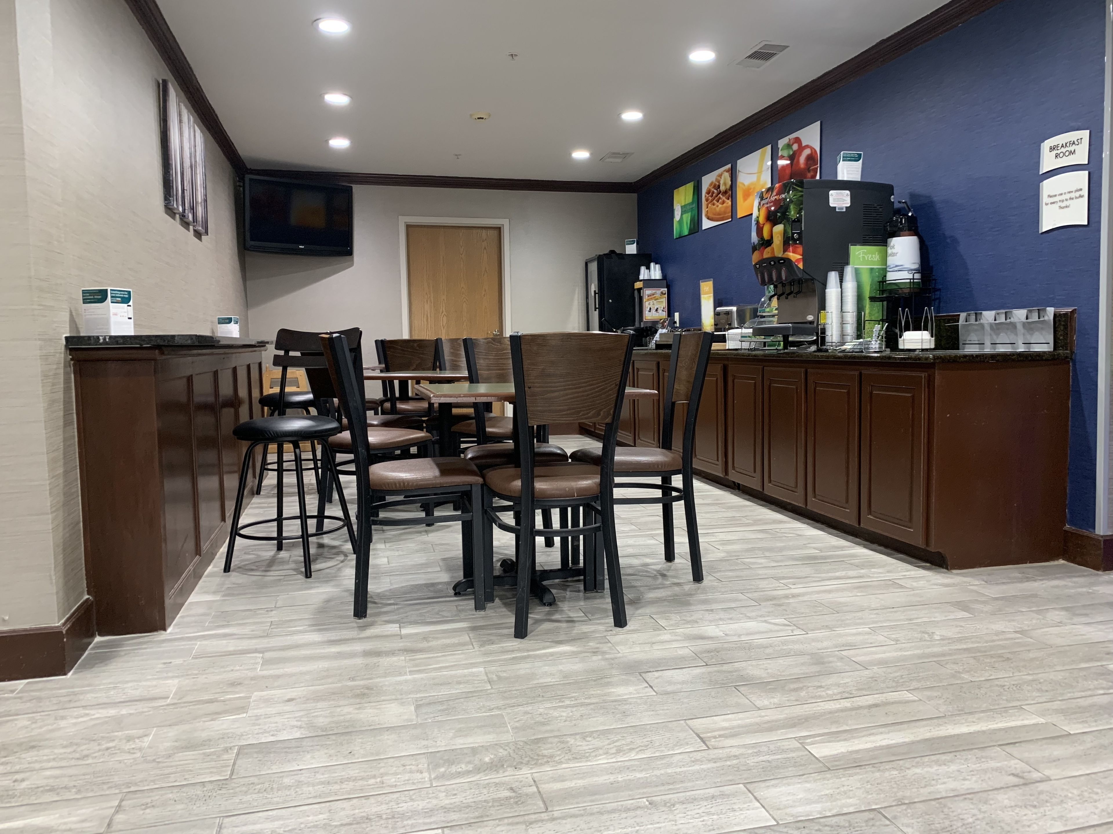 A breakfast area with wooden tables and chairs, a counter with a coffee machine, and a wall with fruit images.