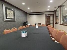 A conference room with a long table, chairs, a framed picture on the wall, and a door with glass panels.