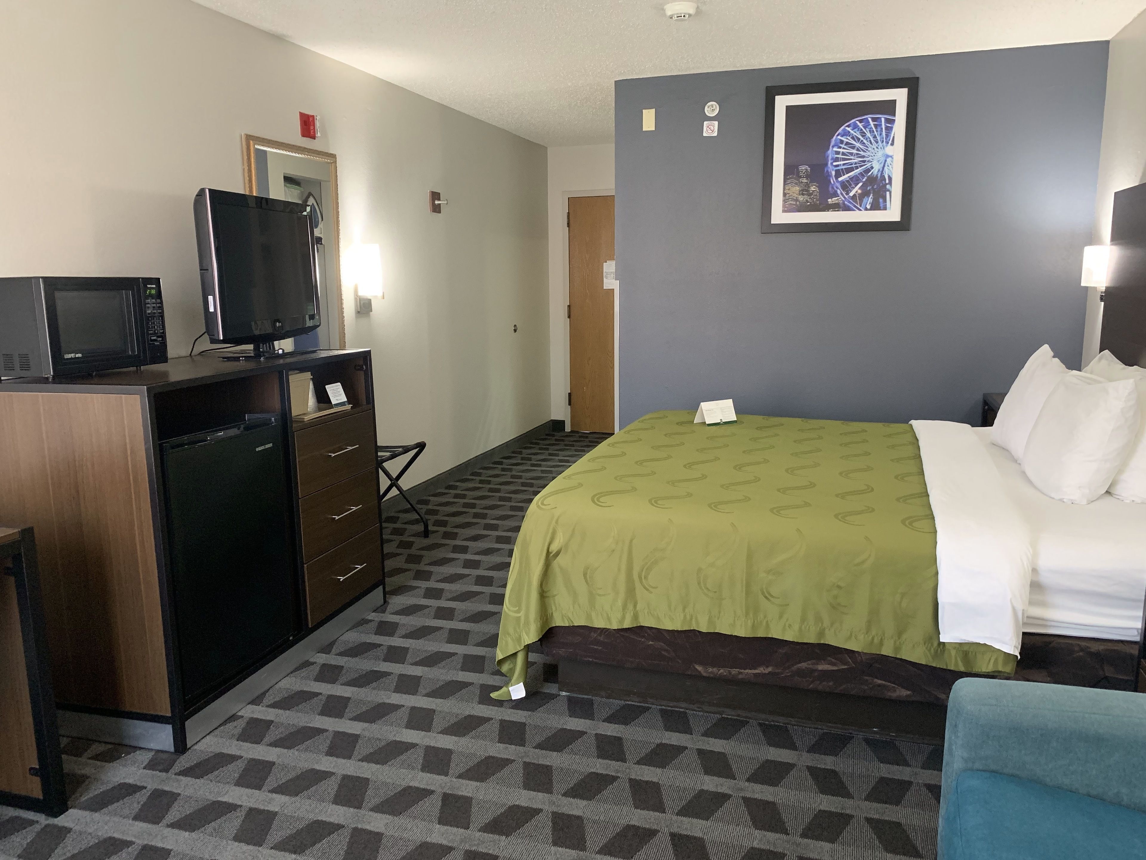 A hotel room with a bed, a desk with a TV, a microwave, and a refrigerator.