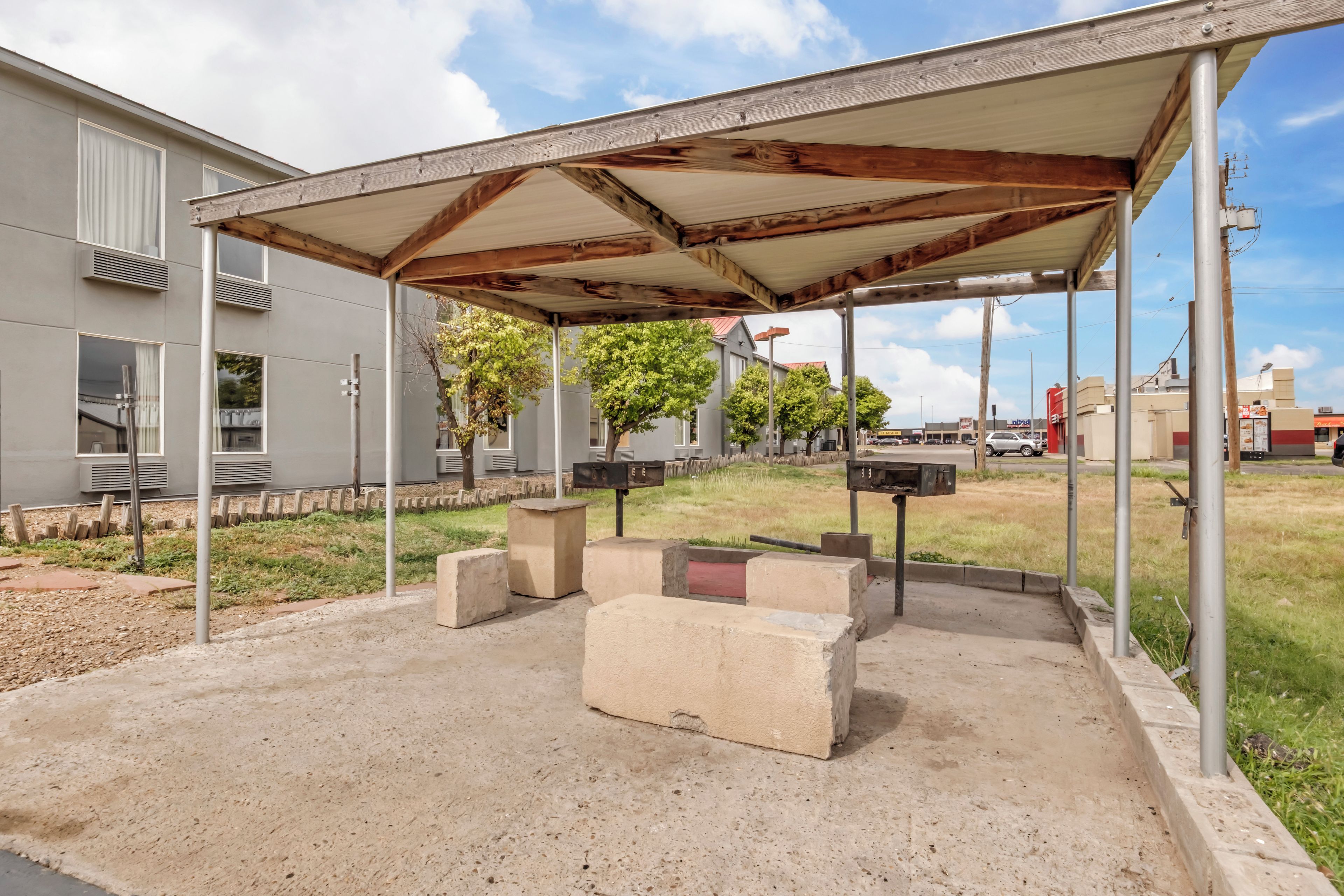 Un espacio de estar al aire libre cubierto con bancos de concreto y estructura de techo metálica.
