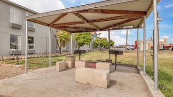 Un espacio de estar al aire libre cubierto con bancos de concreto y estructura de techo metálica.