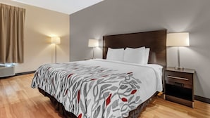A hotel room with a bed, two bedside lamps, a wooden nightstand, and an air conditioning unit. - Red Roof Inn Dumas (Dumas)