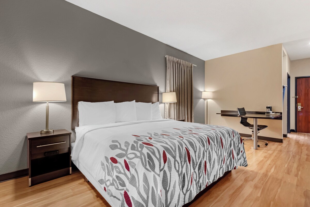 A hotel room with a bed, bedside tables, lamps, a desk with a chair, and a door.