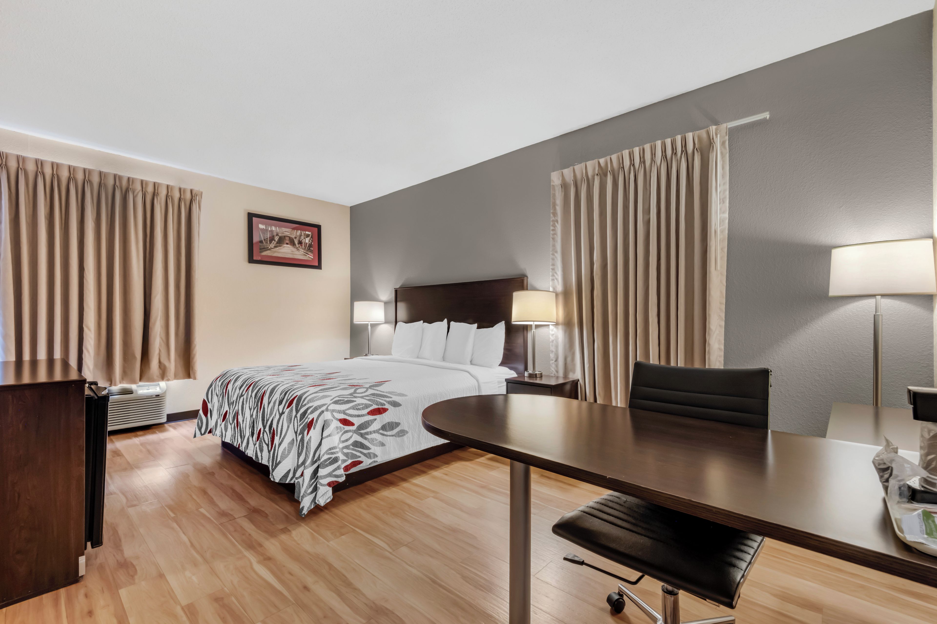 A hotel room with a bed, bedside tables, a desk, a chair, and a lamp.
