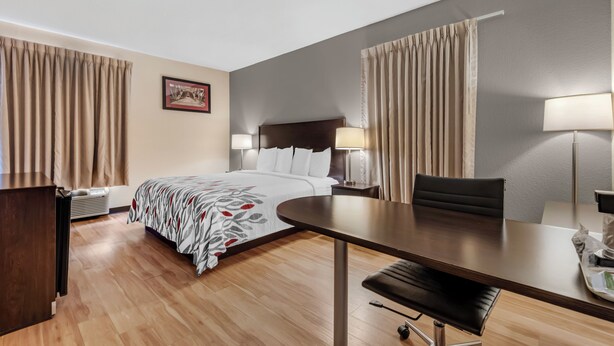 A hotel room with a bed, bedside tables, a desk, a chair, and a lamp. - Red Roof Inn Dumas (Dumas)