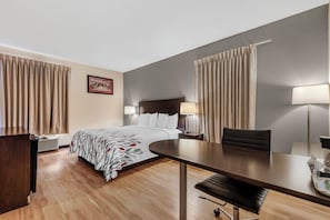 A hotel room with a bed, bedside tables, a desk, a chair, and a lamp. - Red Roof Inn Dumas (Dumas)