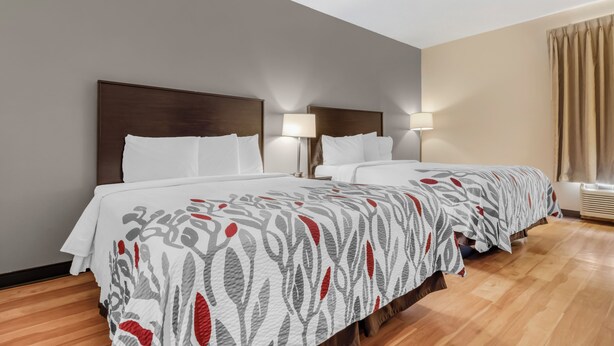 A hotel room with two beds, a wooden floor, and a window with curtains. - Red Roof Inn Dumas (Dumas)