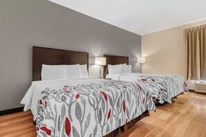 Een hotelkamer met twee bedden, een houten vloer en een raam met gordijnen.