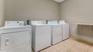 A laundry room with three Whirlpool front-loading washers and a small shelf. - Red Roof Inn Dumas (Dumas)