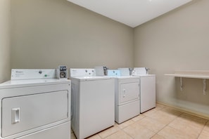 A laundry room with three Whirlpool front-loading washers and a small shelf. - Red Roof Inn Dumas (Dumas)