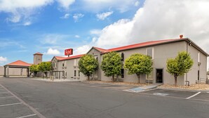 A hotel with a red roof, multiple trees in front, and a clear sky. - Red Roof Inn Dumas (Dumas)