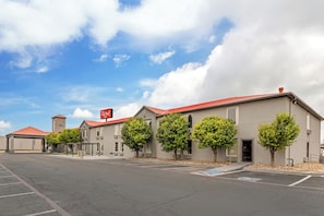 A hotel with a red roof, multiple trees in front, and a clear sky. - Red Roof Inn Dumas (Dumas)